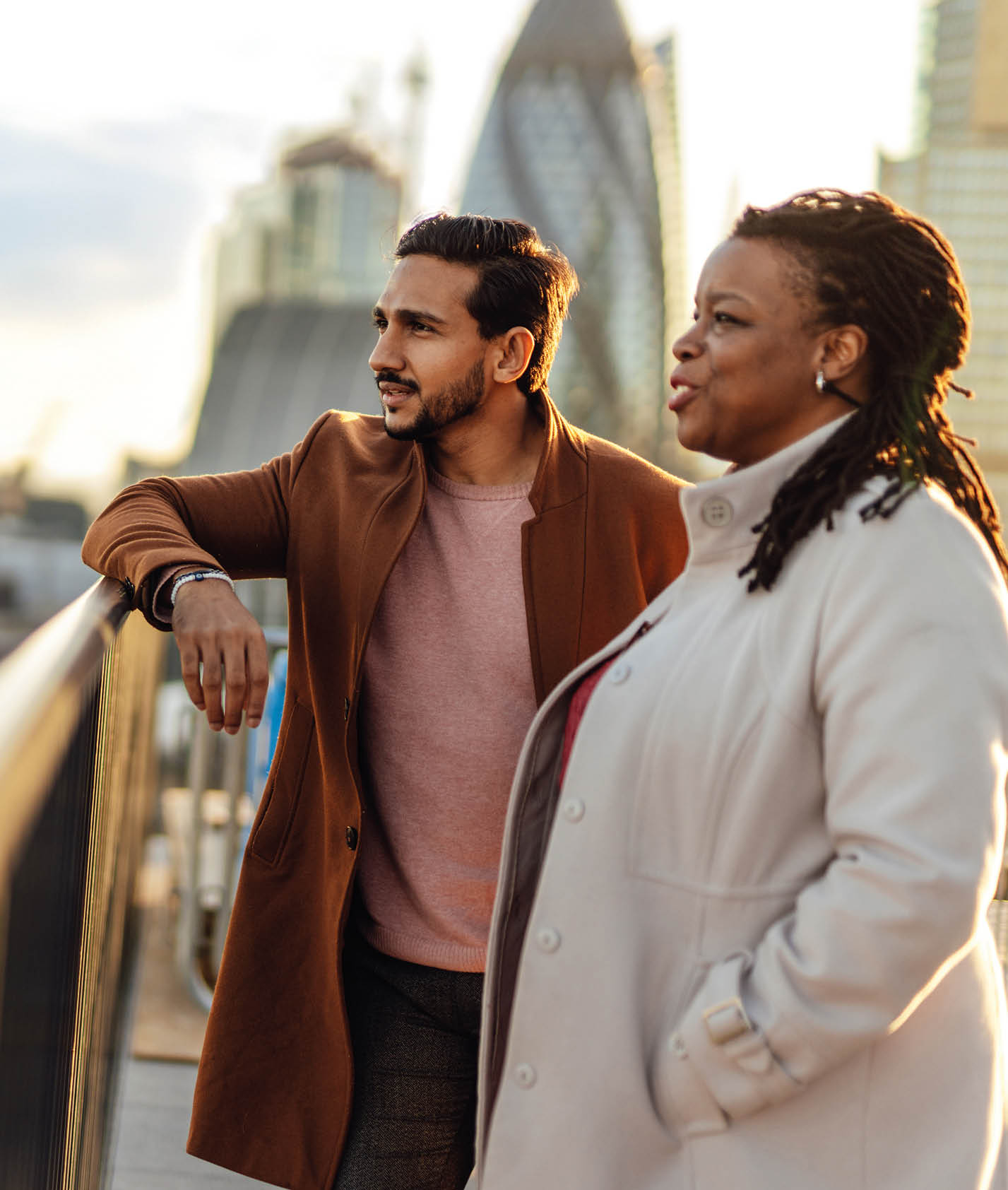 Mixed race businessman and African businesswoman discussing business plans together at rooftop garden in a high-rise office building. They're talking, planning and thinking strategy and discussing business strategy at urban balcony overlooking city, Liverpool, London.
