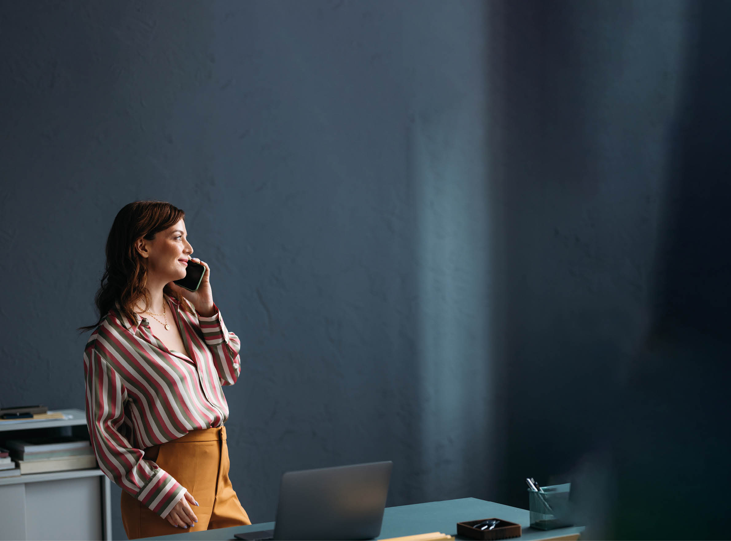 Confident businesswoman converses on smartphone in office, casual style, focused and tranquil mood, contemporary workspace.