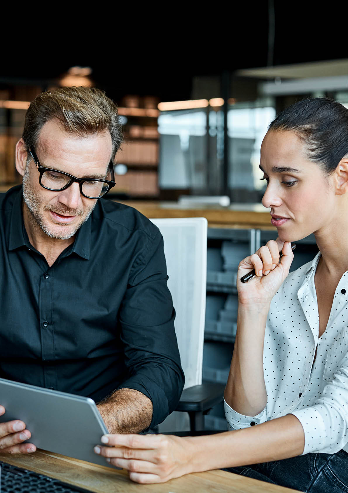 Male and female colleagues looking at tablet PC. Business people are working at desk. They are sitting in textile factory.